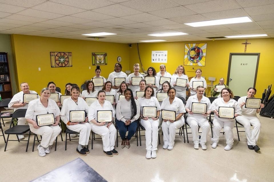 Women in white uniforms holding framed certificates at a program completion ceremony